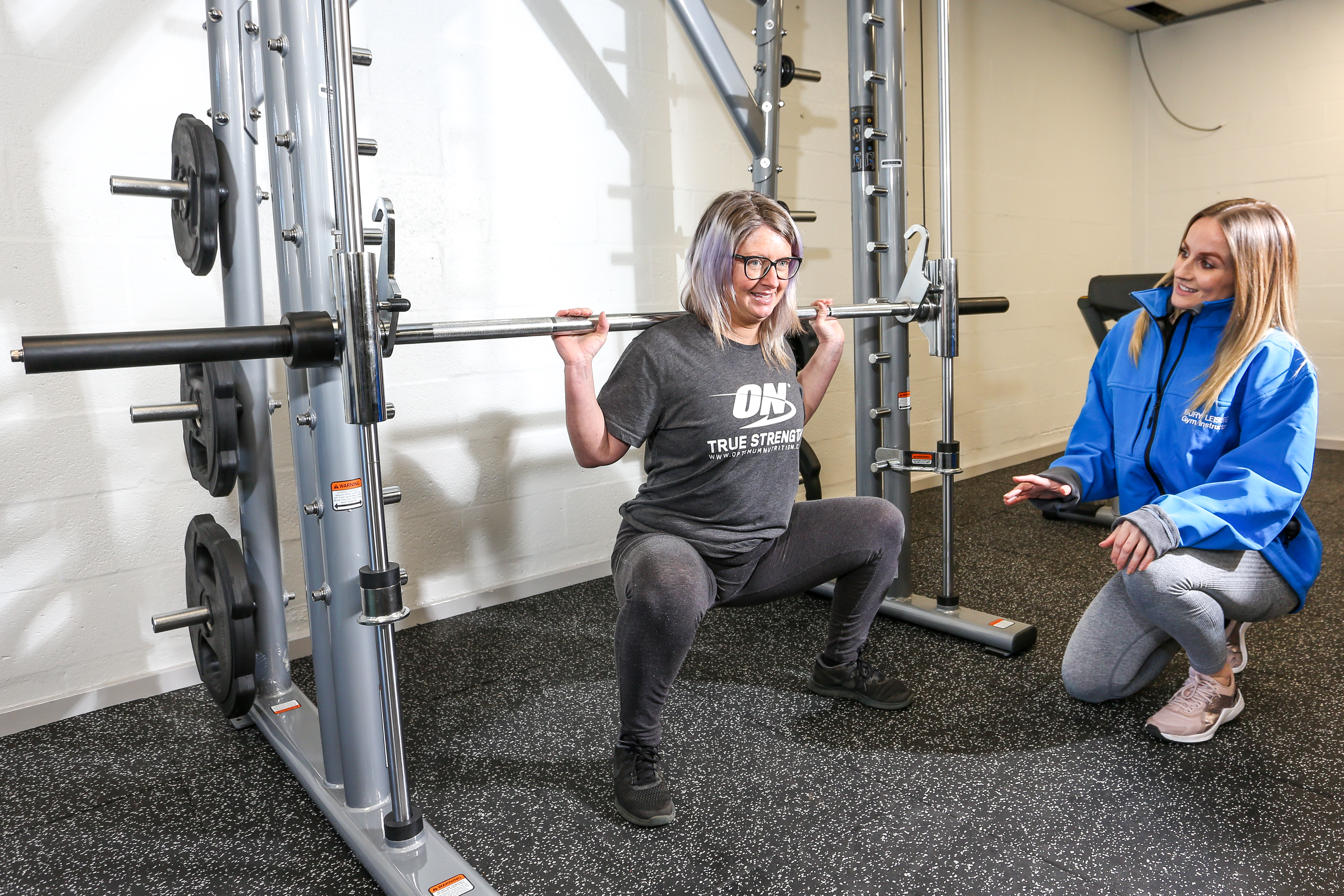 Woman lifting a weight in a gym with another woman watching her