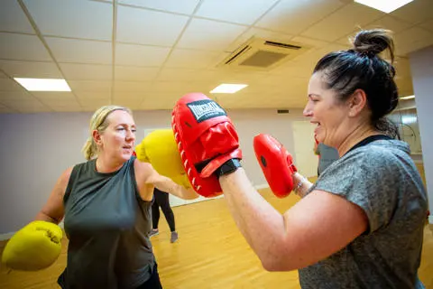 Women wearing boxing gloves hitting the hand of another woman wearing boxing gloves