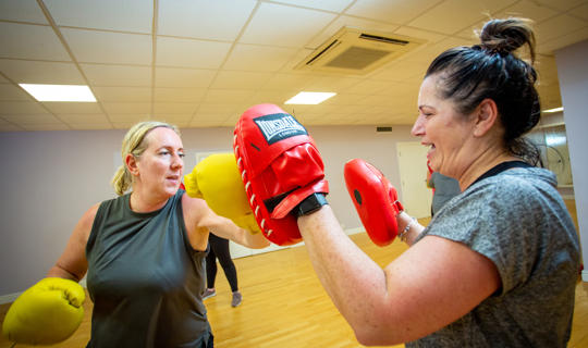 Women wearing boxing gloves hitting the hand of another woman wearing boxing gloves