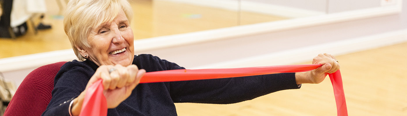Women sat in a chair holding an exercise band taking part in a gentle exercise class at Castle Leisure Centre