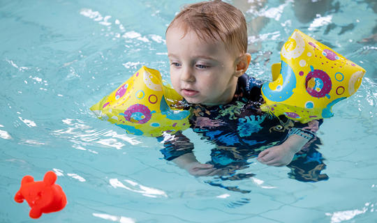 Child with arm bands floating in the pool