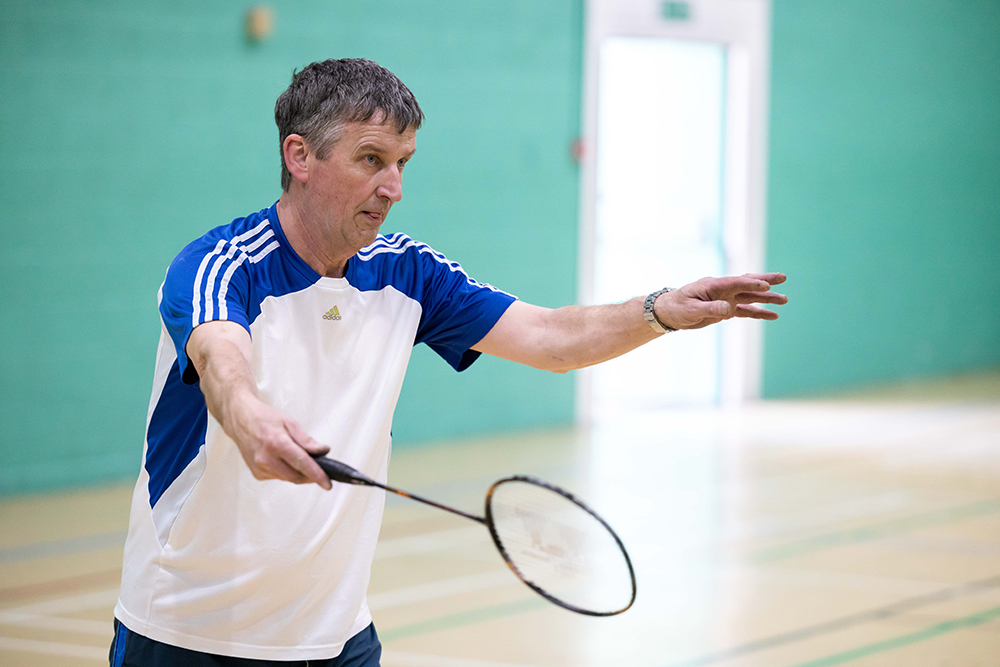 Man holding a badminton racquet in a sports hall