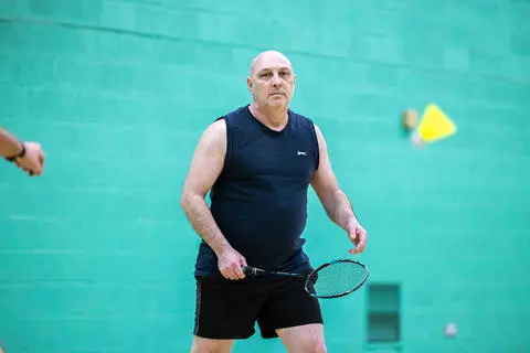 A man playing holding a badminton racquet  a sports hall