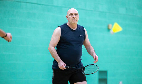 A man playing holding a badminton racquet  a sports hall