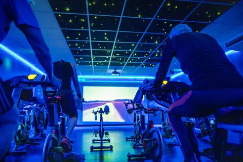 A group of people on spin bikes following an on-screen virtual spin class