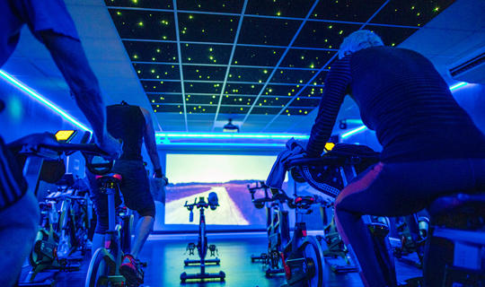 A group of people on spin bikes following an on-screen virtual spin class
