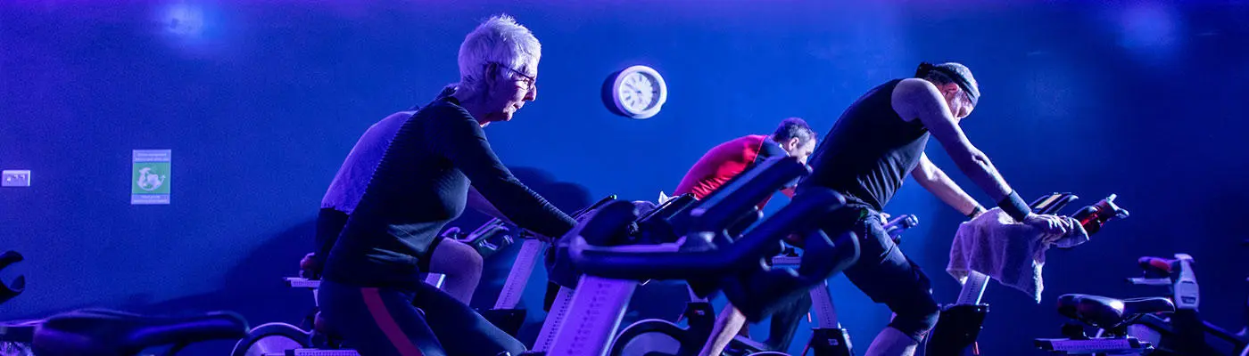 Three people on exercise bikes in a room with blue lighting